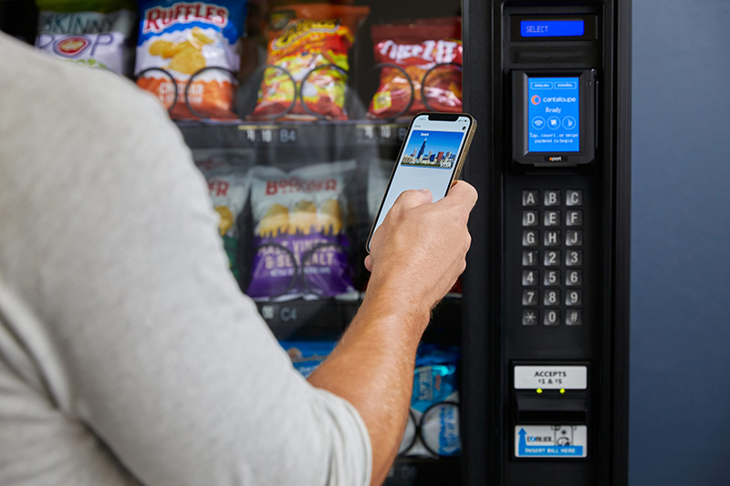 Woman pays with her mobile wallet at a vending machine card reader.