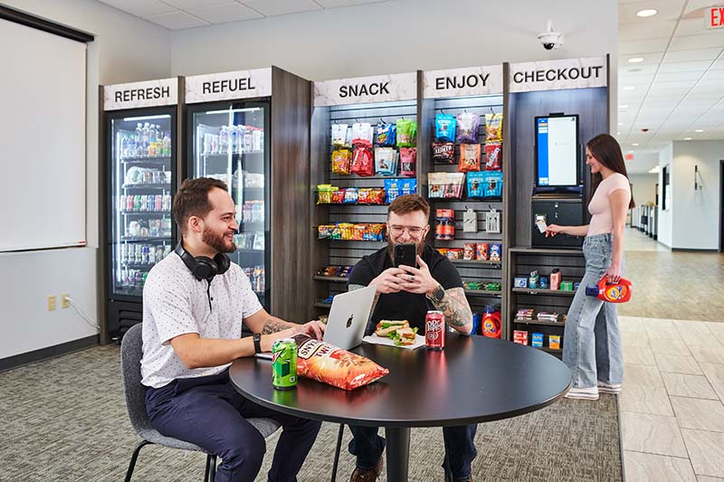 Residents sit around a small table in front of a micro market while a customer purchases items from the market.