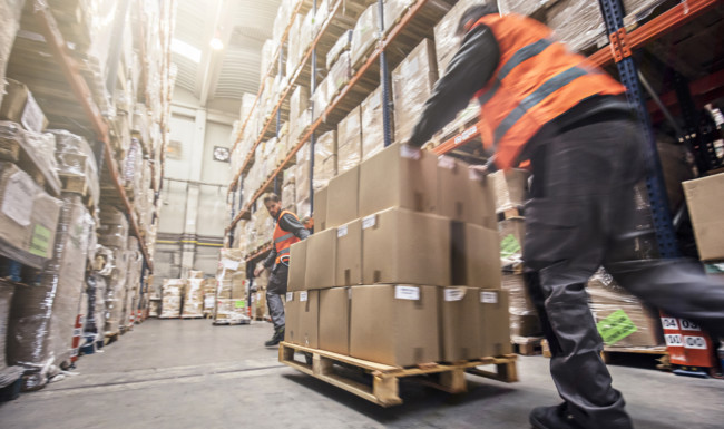 Worker moves a pallet of boxes down a warehouse hall
