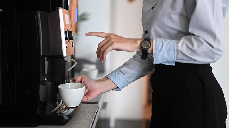Woman makes a coffee during a break at an office coffee machine.