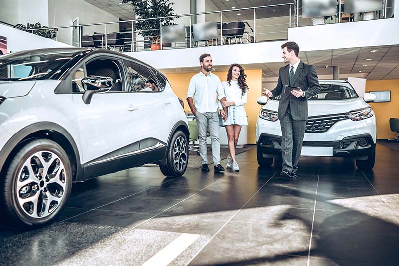 Car dealership salesman leads two customers through the show floor.