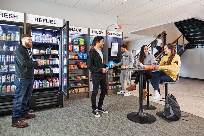 College students gathered around a high top table in front of a fully stocked micro market.