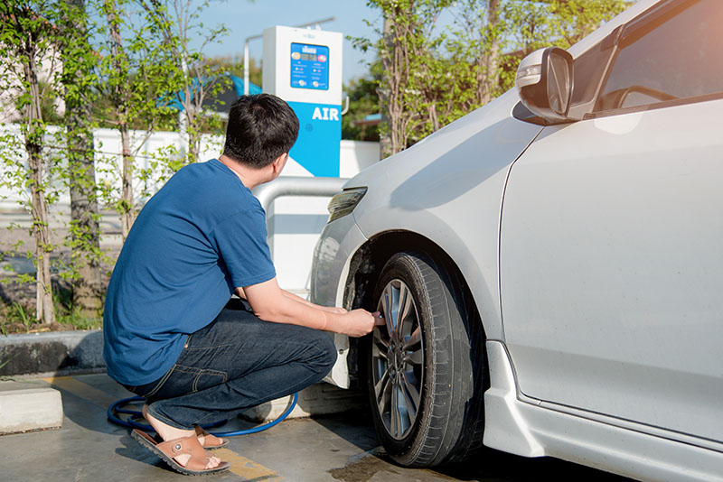 A man refills the front driver's side tire of his car at a service station air pump.