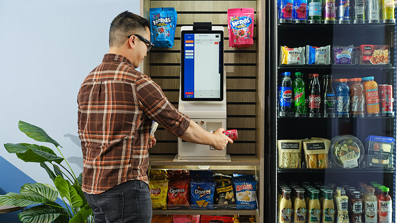 A young man scans a beverage at a Go Plus100 in a small micro market.