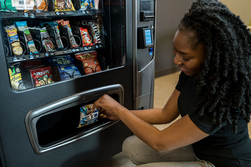 A woman pulls a bag of chips from a vending machine.